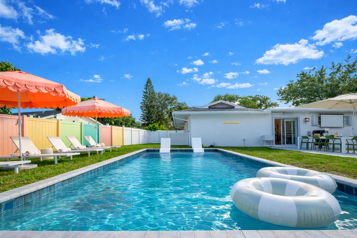 A sun-drenched Palm Beach oasis—brand-new heated saltwater pool with chic in-pool loungers, plush sunbeds, and iconic peach umbrellas, all set within a private, resort-style backyard made for long, lazy afternoons.