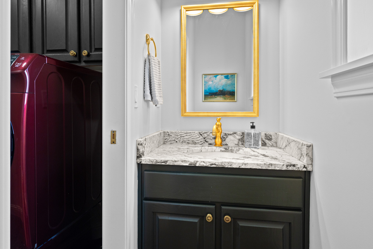 The thoughtfully finished powder room features gorgeous vanity, rich cabinetry, gold-toned accents, and a polished decorative mirror.