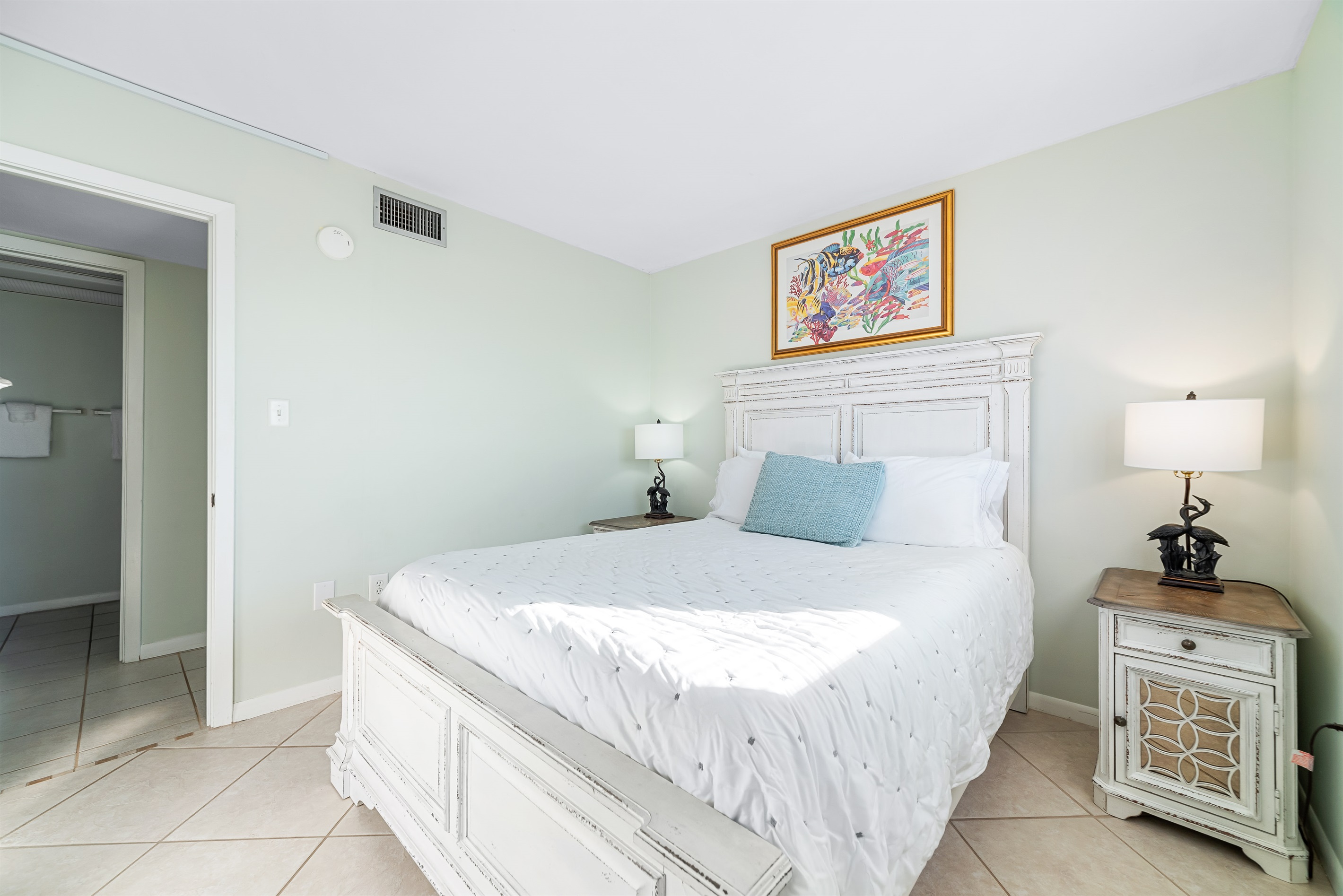 Comfortable queen-size bed with crisp white linens, flanked by matching nightstands and lamps, providing a cozy and inviting space.