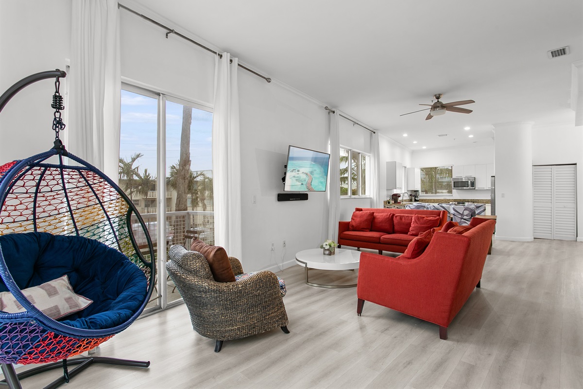 Huge sunny corner living room with two sofas, a daybed, and a swing chair. Private balcony with city and waterway views.
