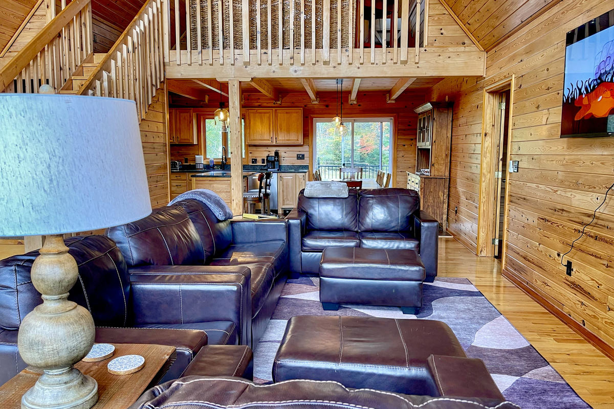 Inviting living area with comfortable leather seating, warm wood interiors, and an open layout connecting the kitchen, dining area, and upstairs loft bedroom.