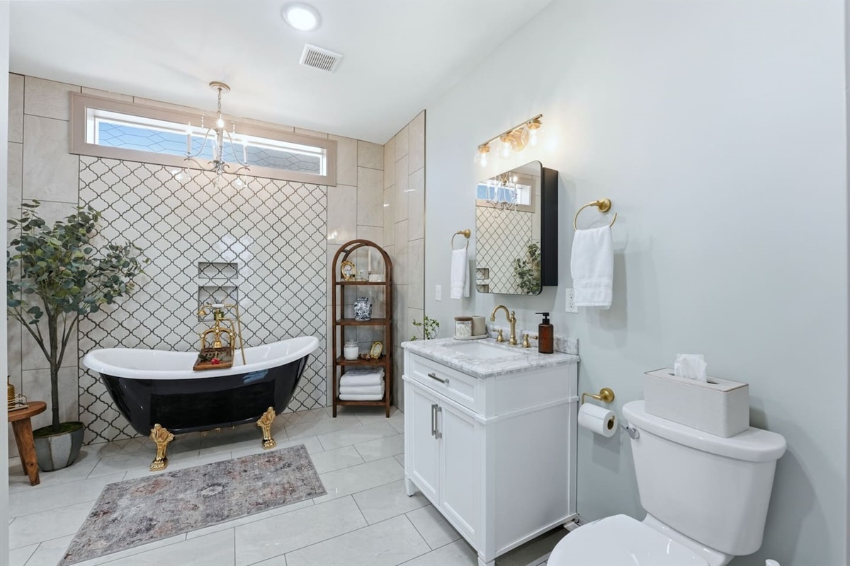 Luxurious spa-inspired bathroom featuring a stunning freestanding soaking tub with gold accents, elegant tilework, and a bright vanity—perfect for relaxing after a long day.