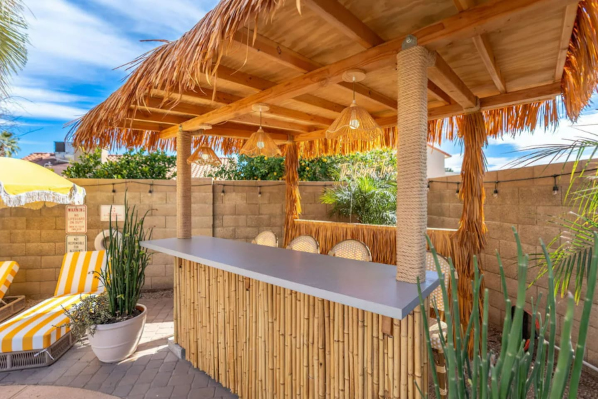 Tropical outdoor bar with thatched roof, pendant lighting, and desert plants—the perfect spot for cocktails and entertaining.