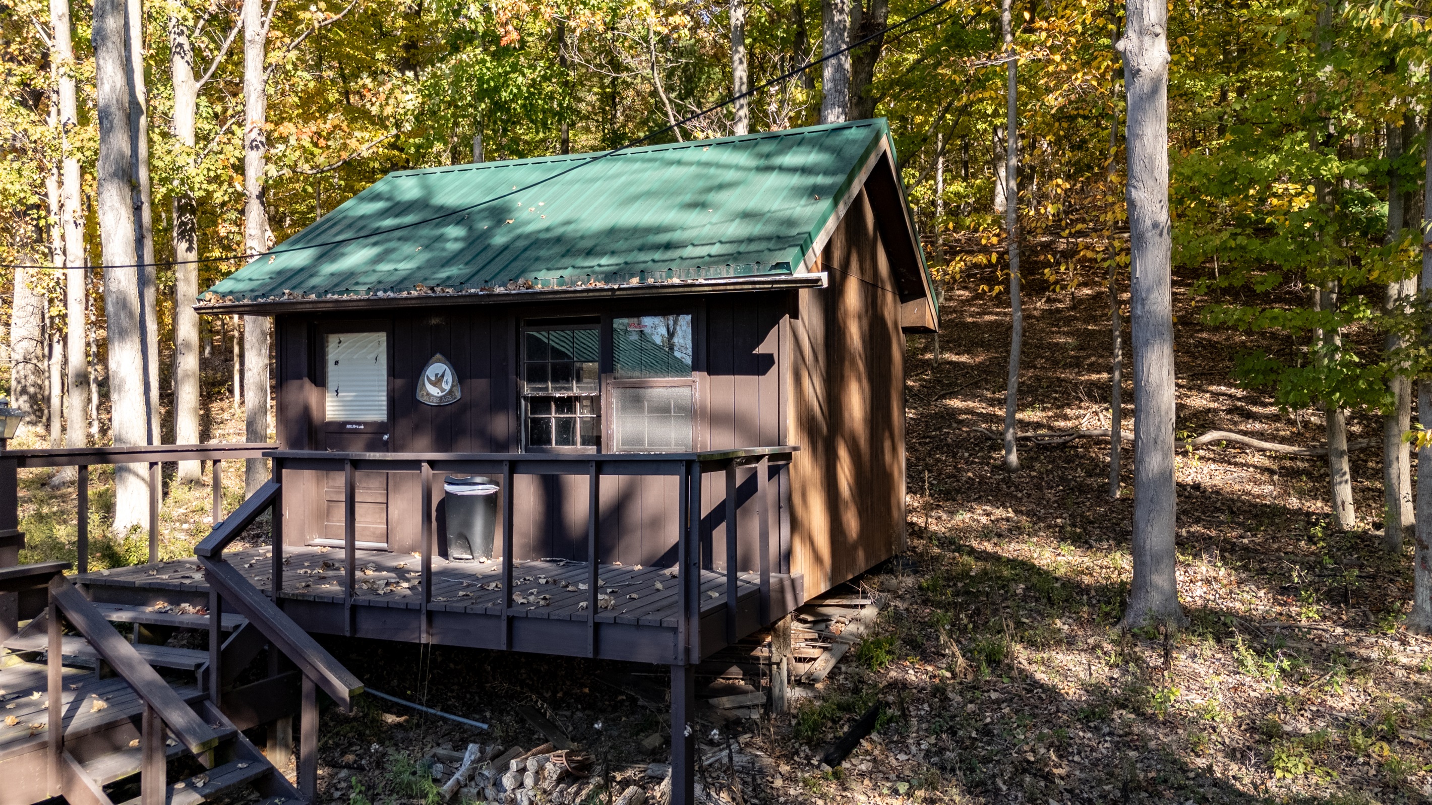 Cabin deck shown from the side with wood siding and tree coverage.