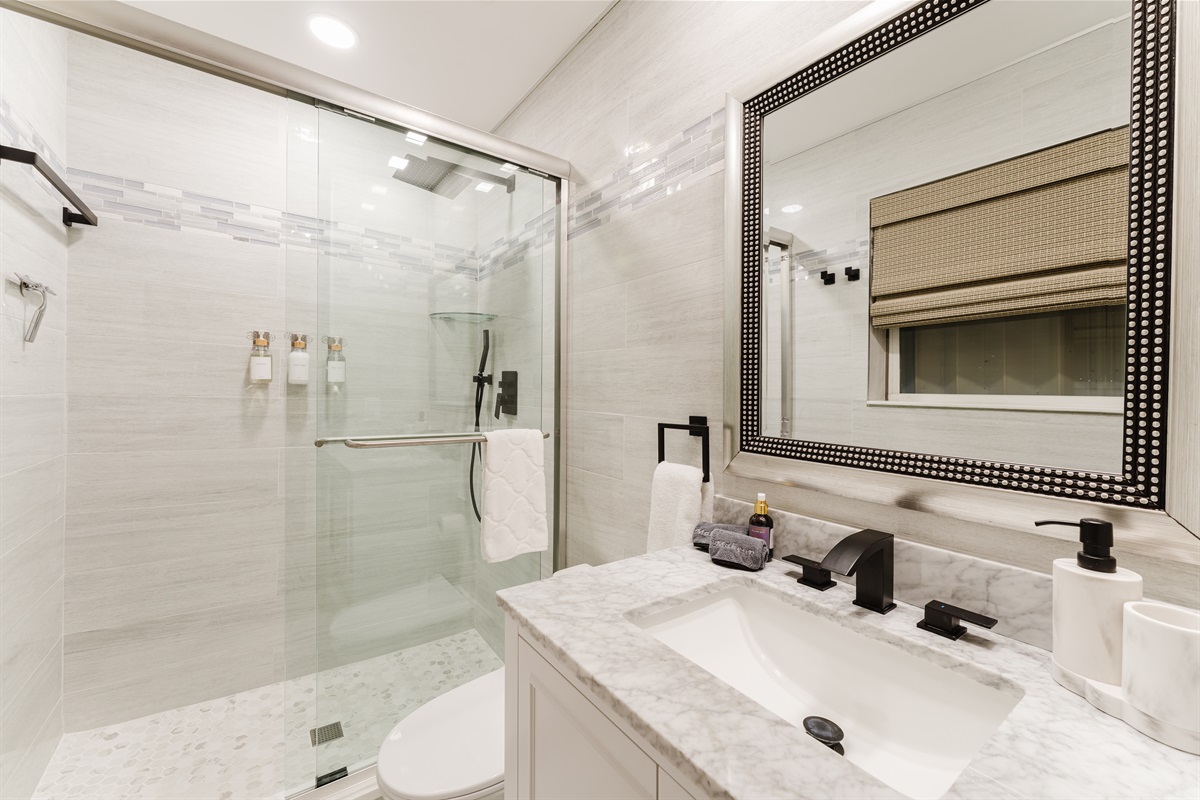 Private spa-style ensuite with a glass-enclosed walk-in shower, marble vanity, matte black fixtures, and hotel-quality finishes.