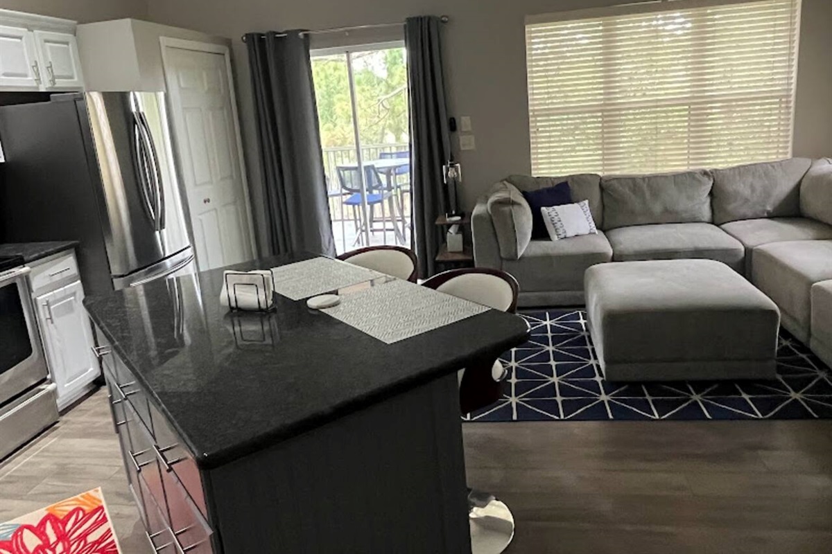 Open kitchen and living space with updated finishes, breakfast bar seating, and natural light from the balcony doors.