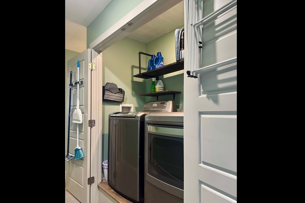 Fully equipped laundry area with detergent, bleach, stain remover, and mounted cleaning tools including mop, broom, duster, and extra mop pads.
