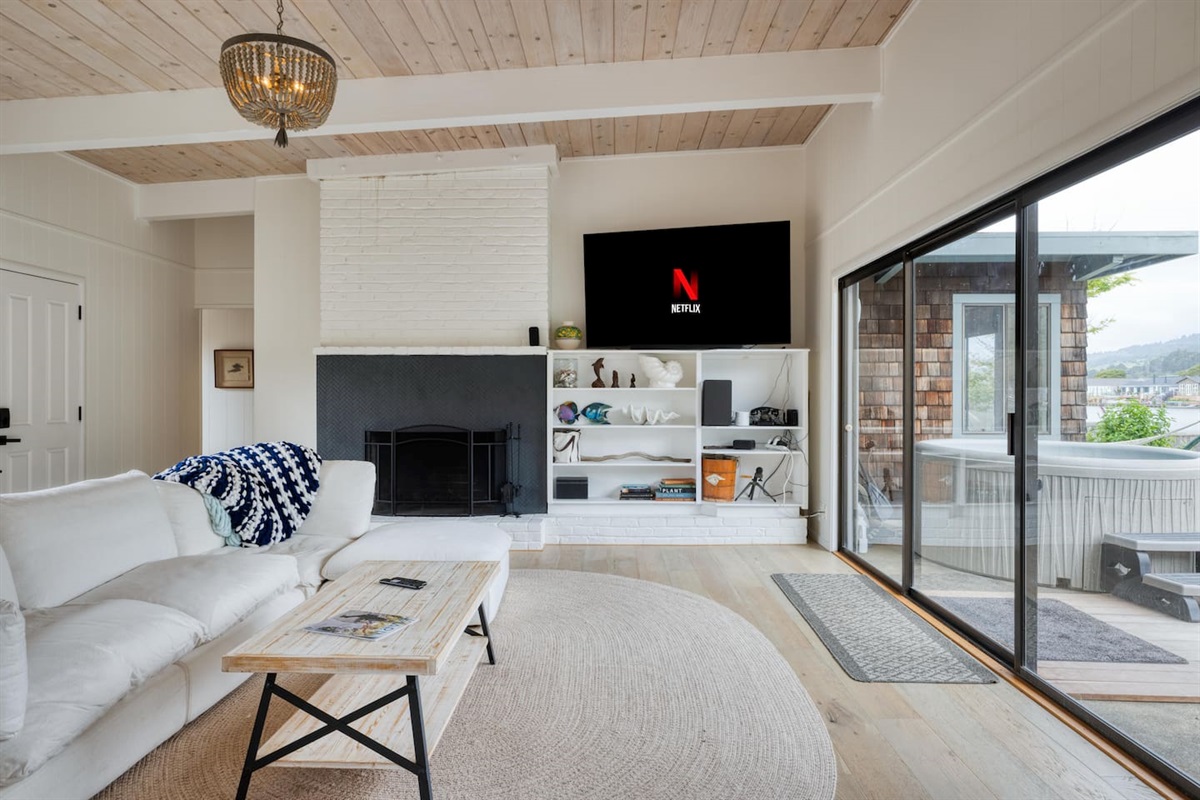 - Comfortable living area with fireplace, TV, and built in shelving decor  
- Sliding glass doors open directly to the patio and hot tub area outside  
- Soft neutral tones create a calming, welcoming atmosphere for guests  
