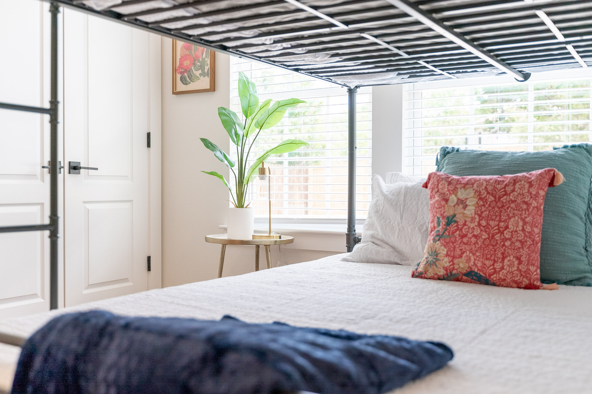 Airy primary bedroom with soft linens, colorful throw pillows, and garden views.