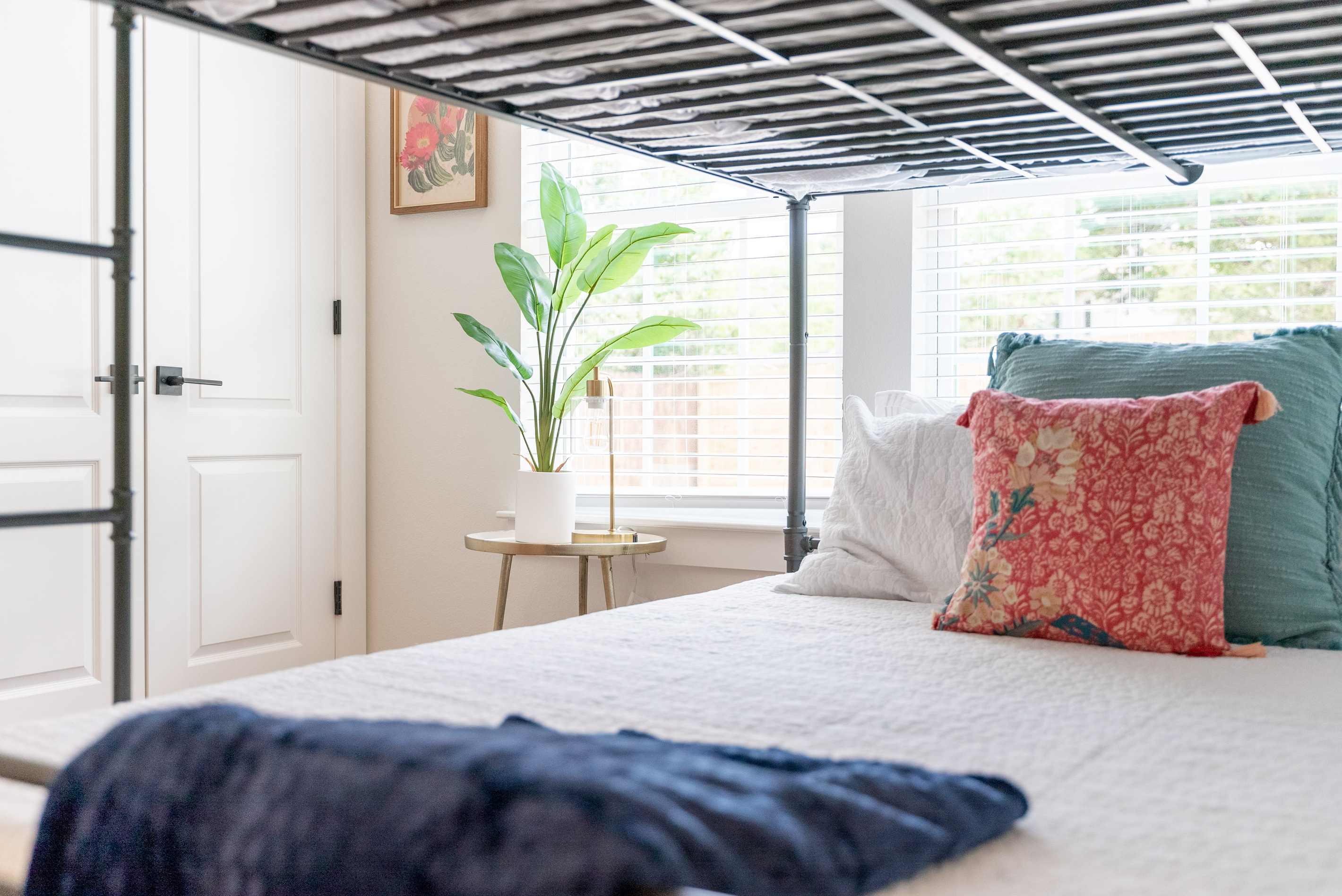 Airy primary bedroom with soft linens, colorful throw pillows, and garden views.