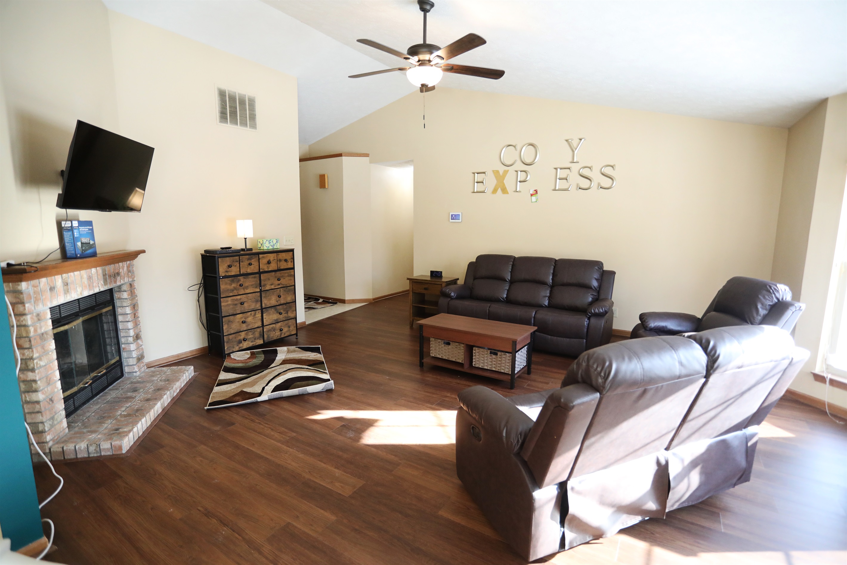 Living Room show Roku TV, fireplace, reclinable single seat, reclinable loveset, and reclinable sofa, coffee table, with bedroom hallway in the background