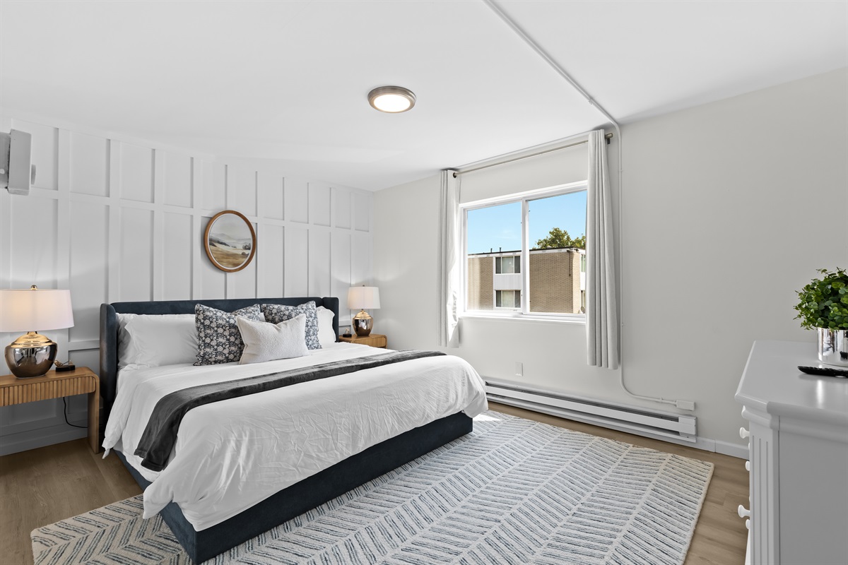 Unwind in a spacious bedroom featuring a plush king bed, crisp linens, and tasteful wall paneling for a refined touch.