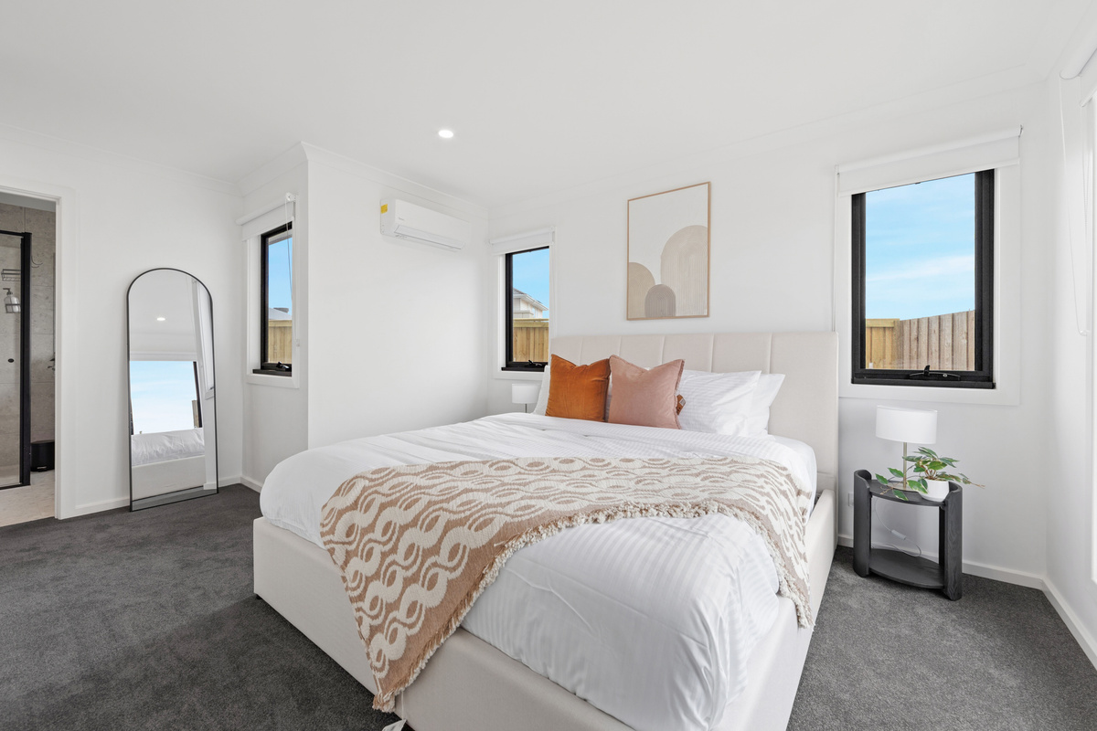 Main bedroom with a king bed in white linen with cushions and a throw, bedside table, mirror and split-system air conditioning.