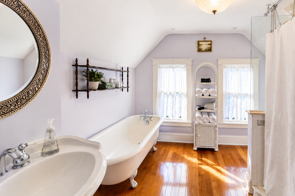 The third floor full bath — a clawfoot tub, original hardwood floors, and lavender walls under a vaulted ceiling. This one might be hard to leave.