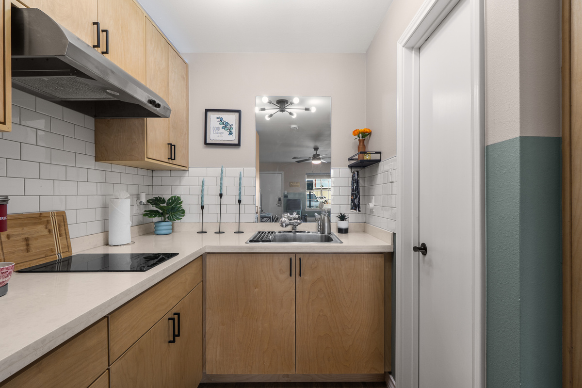 Kitchenette with cooktop, sink, cabinet storage, and the sitting area just beyond.