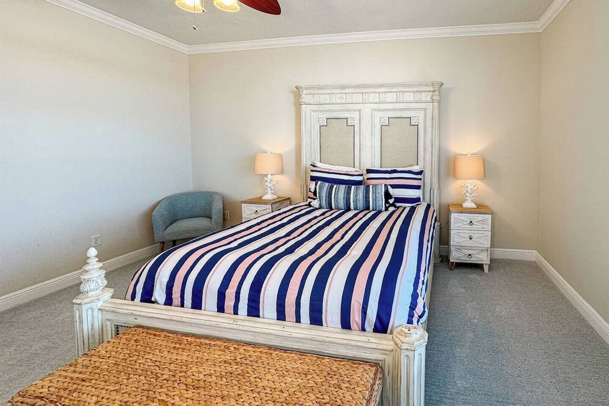 Spacious bedroom with a comfortable bed, fresh linens, and warm lighting. Includes bedside tables, ceiling fan, and cozy seating for a relaxing stay.