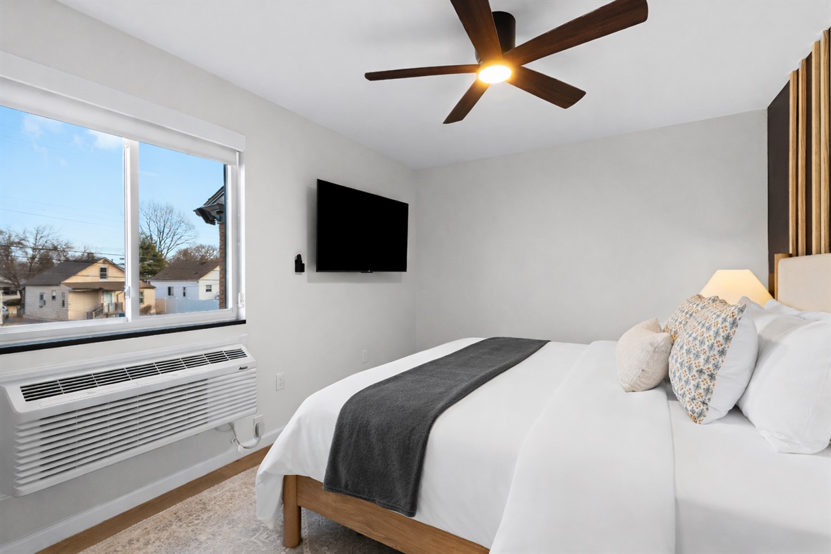 Bright, calming bedroom with plush bed, ceiling fan, and wall-mounted TV—designed for comfort, relaxation, and restful nights.