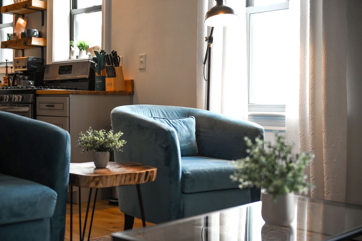 Unwind in an elegant living area with a stylish L-shaped sofa, accent chairs, and a modern coffee table, all enhanced by the warmth of a stunning brick wall.