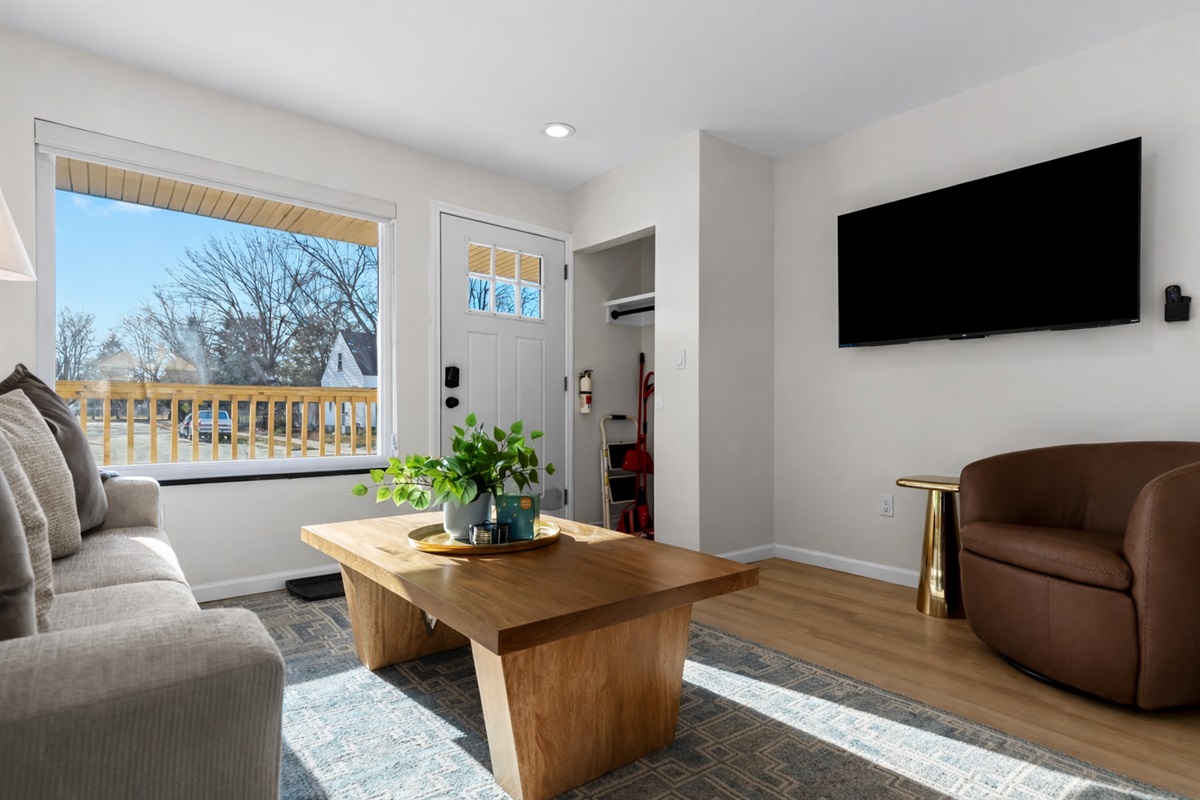 Bright, stylish living room with smart TV, cozy seating, and large windows that fill the space with natural light and fresh neighborhood views.