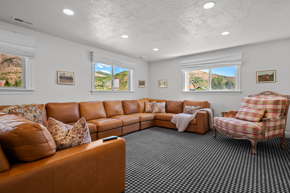 The lower-level family room features a generous sectional, abundant natural light, and wide mountain views for a relaxed yet elevated gathering space.