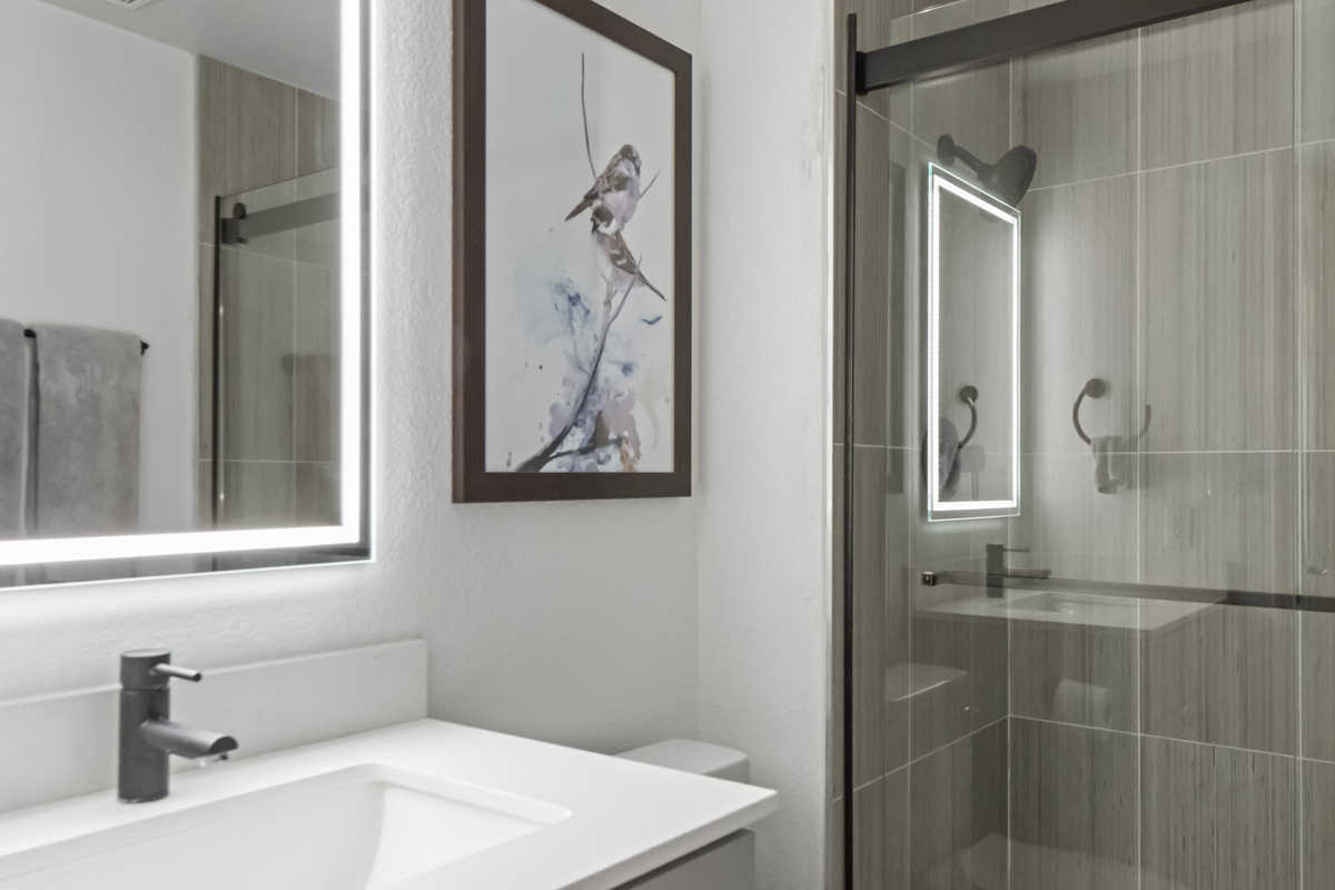 Bright bathroom featuring a modern vanity, large illuminated mirror, and glass-enclosed walk-in shower.