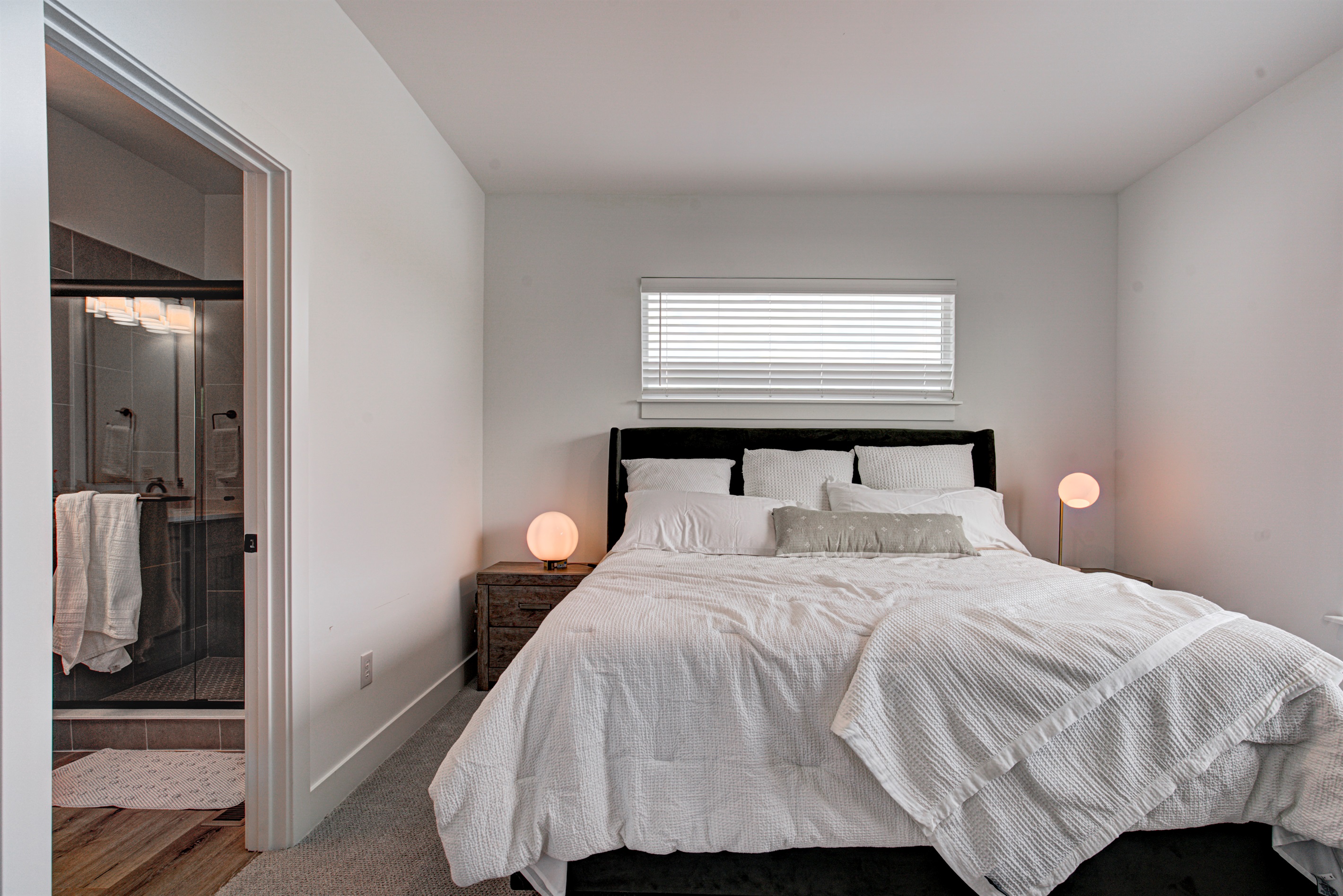 Relax in the serene master bedroom featuring a comfortable king-size bed, soft linens, and cozy pillows. Includes nightstands, lamps, walk-in closet, and full-length mirror for added comfort. 