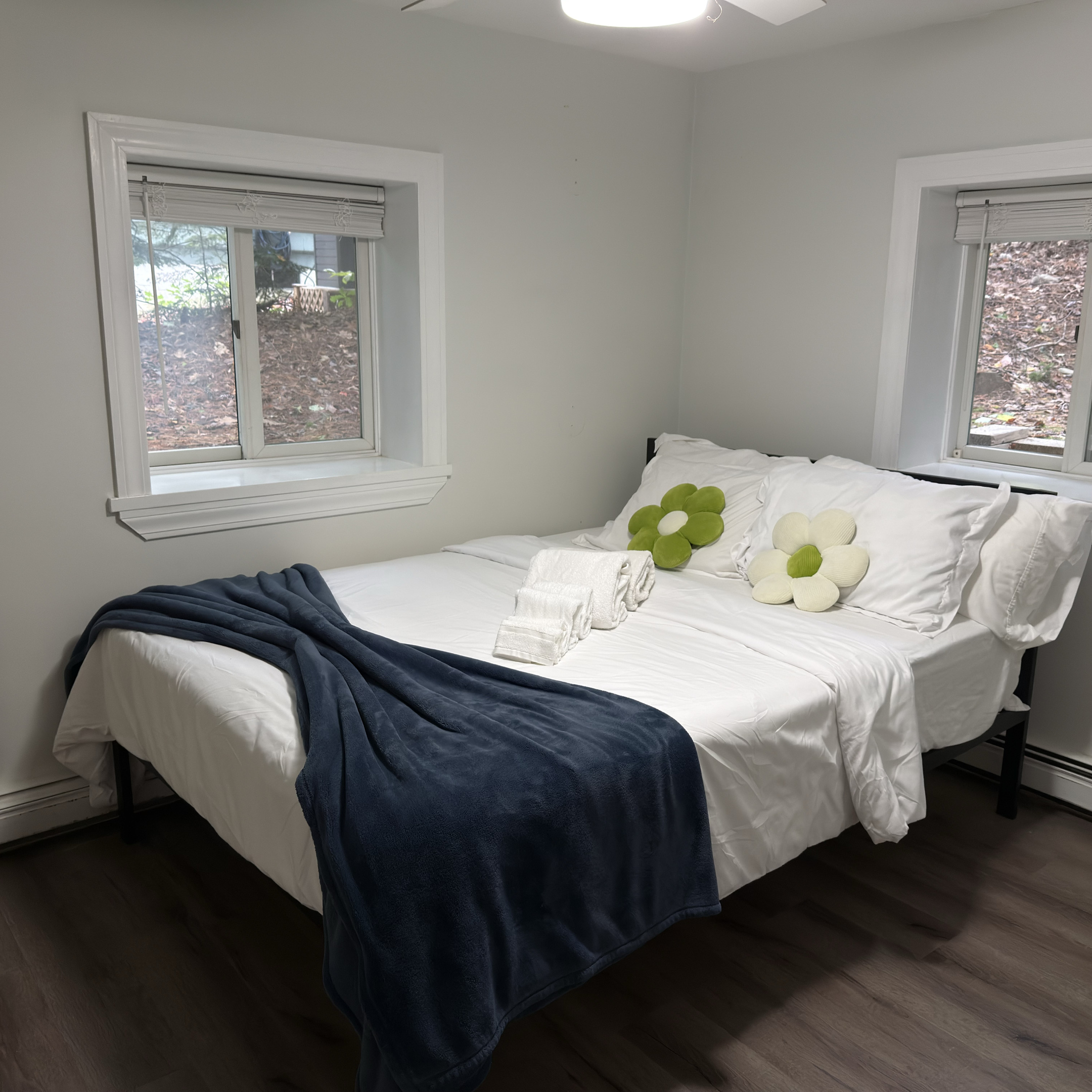 Settle into the queen bedroom with soft white bedding, cheerful accents, and natural light from two windows.