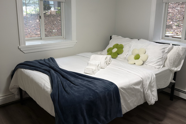 Settle into the queen bedroom with soft white bedding, cheerful accents, and natural light from two windows.
