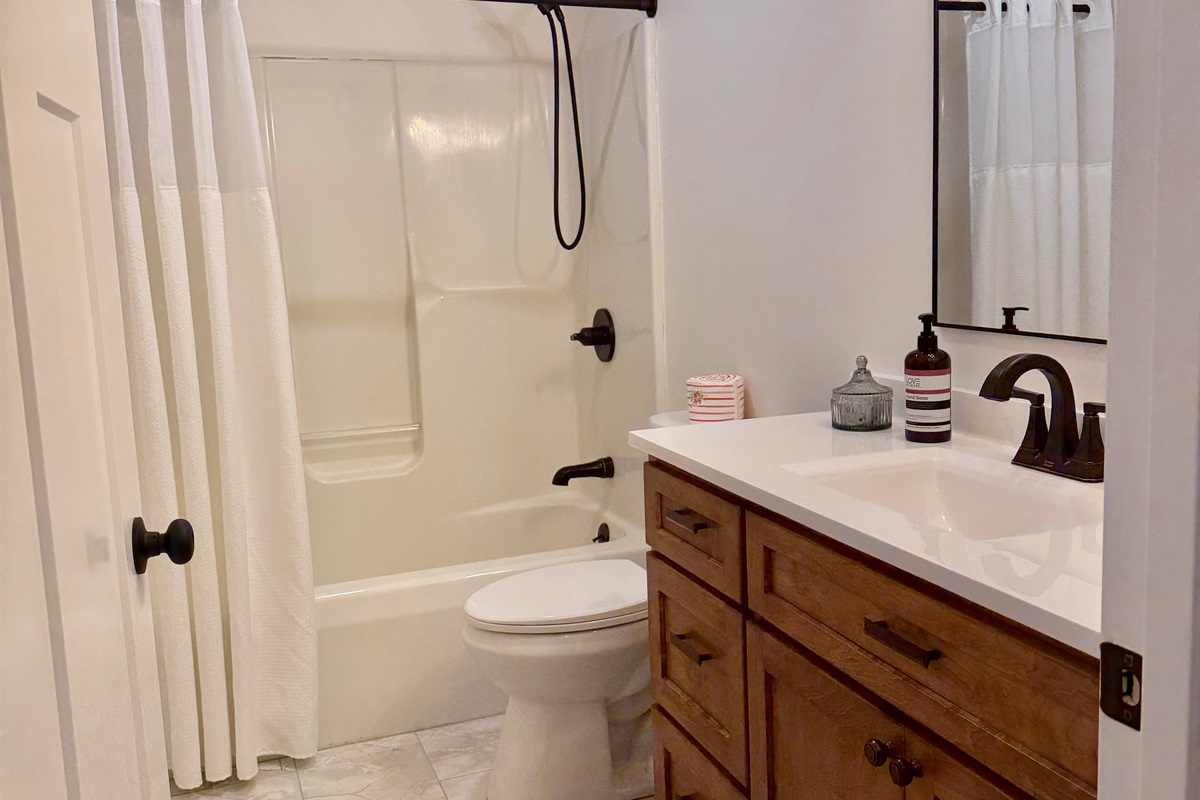 Main bathroom featuring a tub/shower combo, tiled flooring, and custom cabinetry for a clean, modern feel. Includes a hair dryer and conveniently located first aid kit for added comfort and convenience during your stay