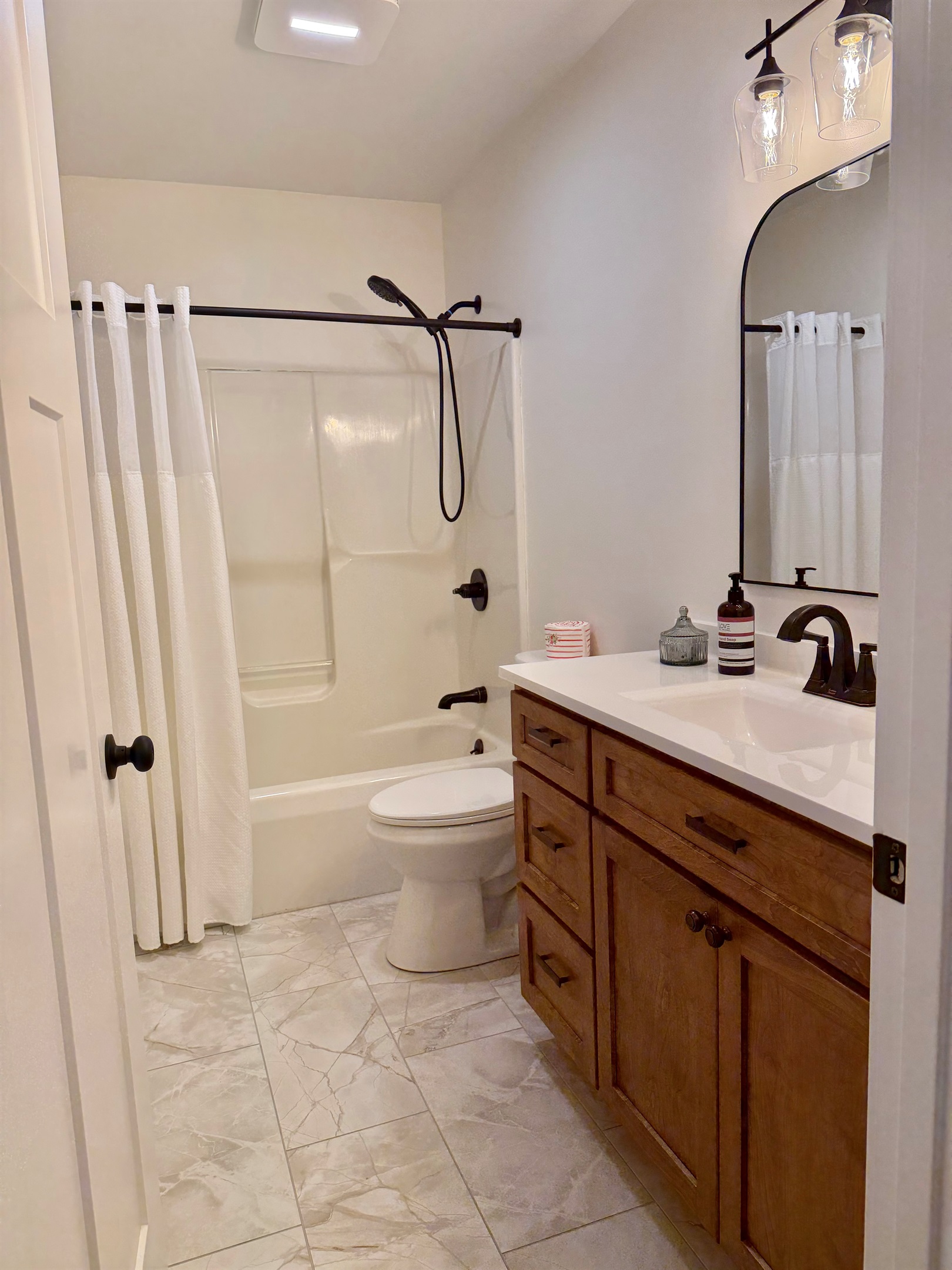 Main bathroom featuring a tub/shower combo, tiled flooring, and custom cabinetry for a clean, modern feel. Includes a hair dryer and conveniently located first aid kit for added comfort and convenience during your stay