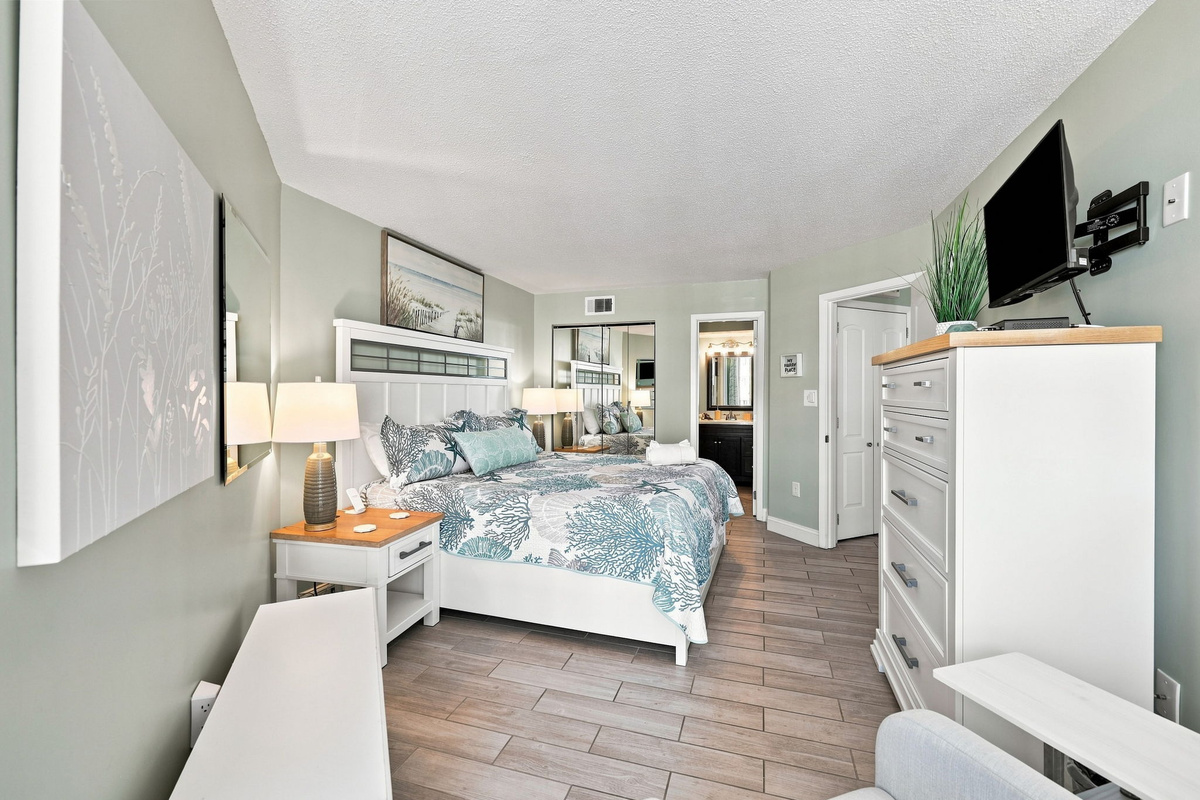 Cozy bedroom retreat complete with inviting coastal linens, matching nightstands, and a wall-mounted TV to unwind after a day in the sun.