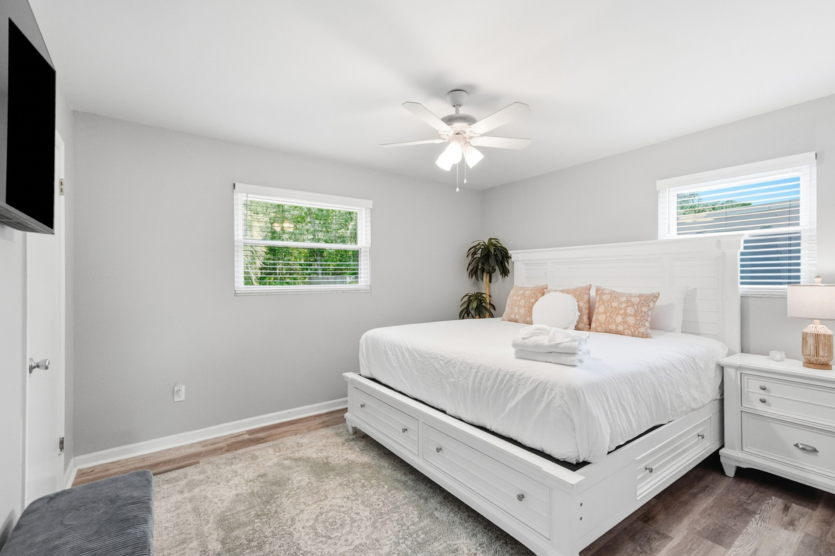 Relax in this bright bedroom with comfortable bedding, a ceiling fan, mounted TV, and built-in bed storage.
