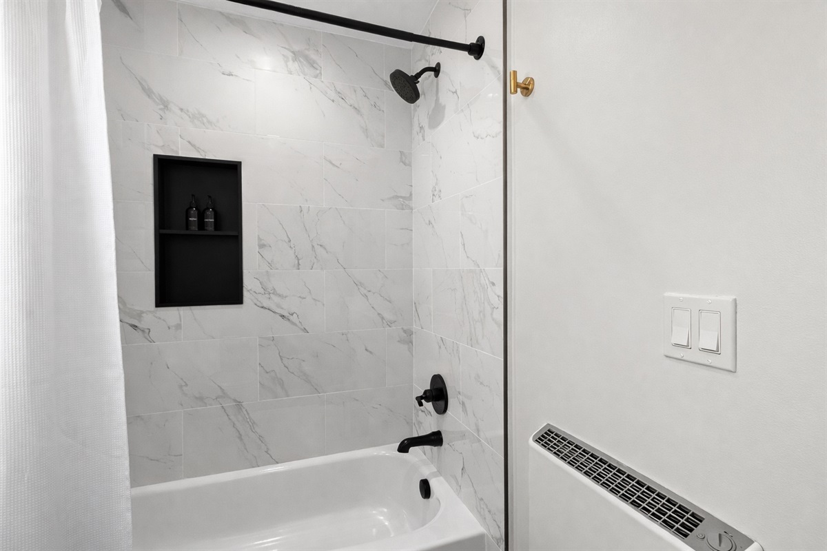 Sleek tub-shower combo with modern tile, matte black fixtures, and built-in storage—clean, stylish, and perfect for a refreshing start or relaxing soak.