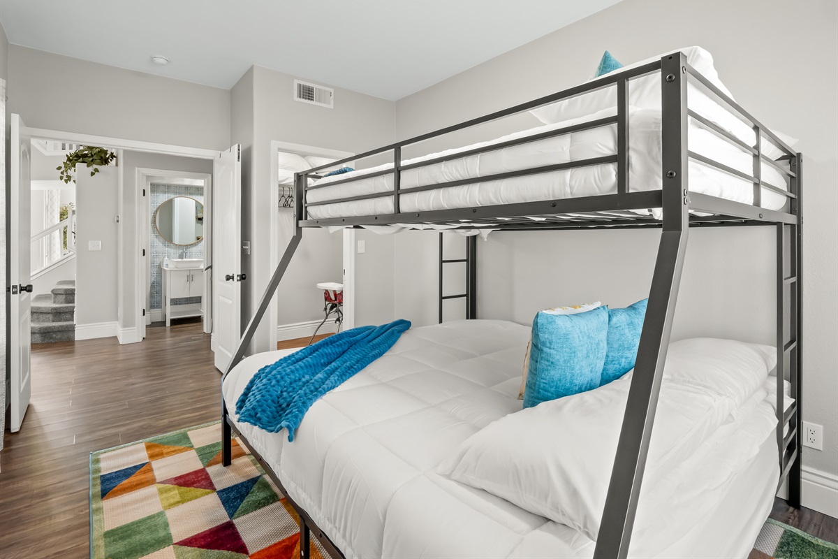 Spacious bunk room with a queen bed below and twin above, soft bedding, and easy access to the hallway bathroom—ideal for kids, teens, or additional guests.