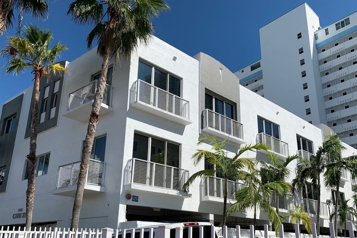 Small townhouse building in classic Miami white with grey accents, framed by palms