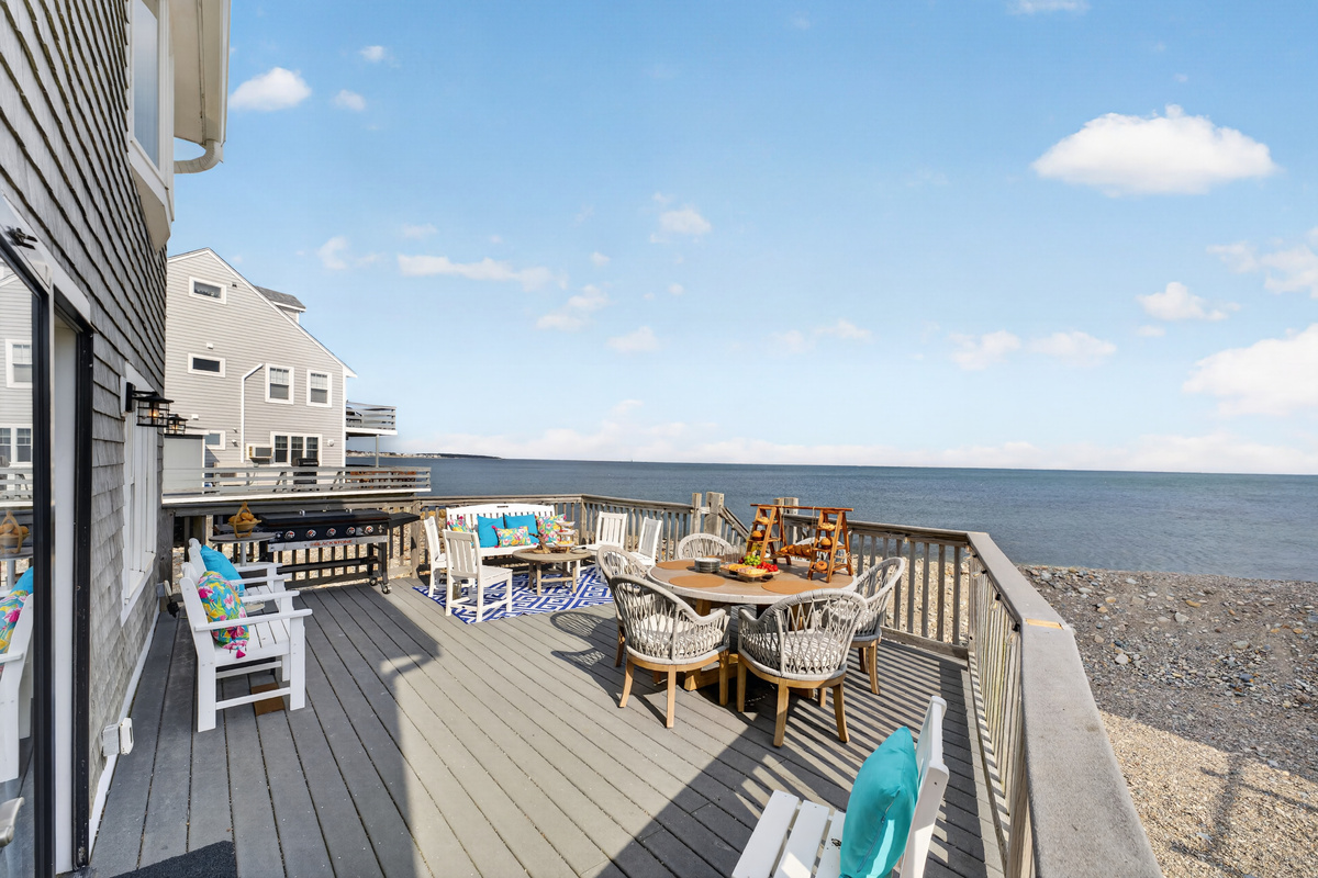 Spacious oceanfront deck with outdoor dining and seating, ideal for enjoying meals with a sea breeze.