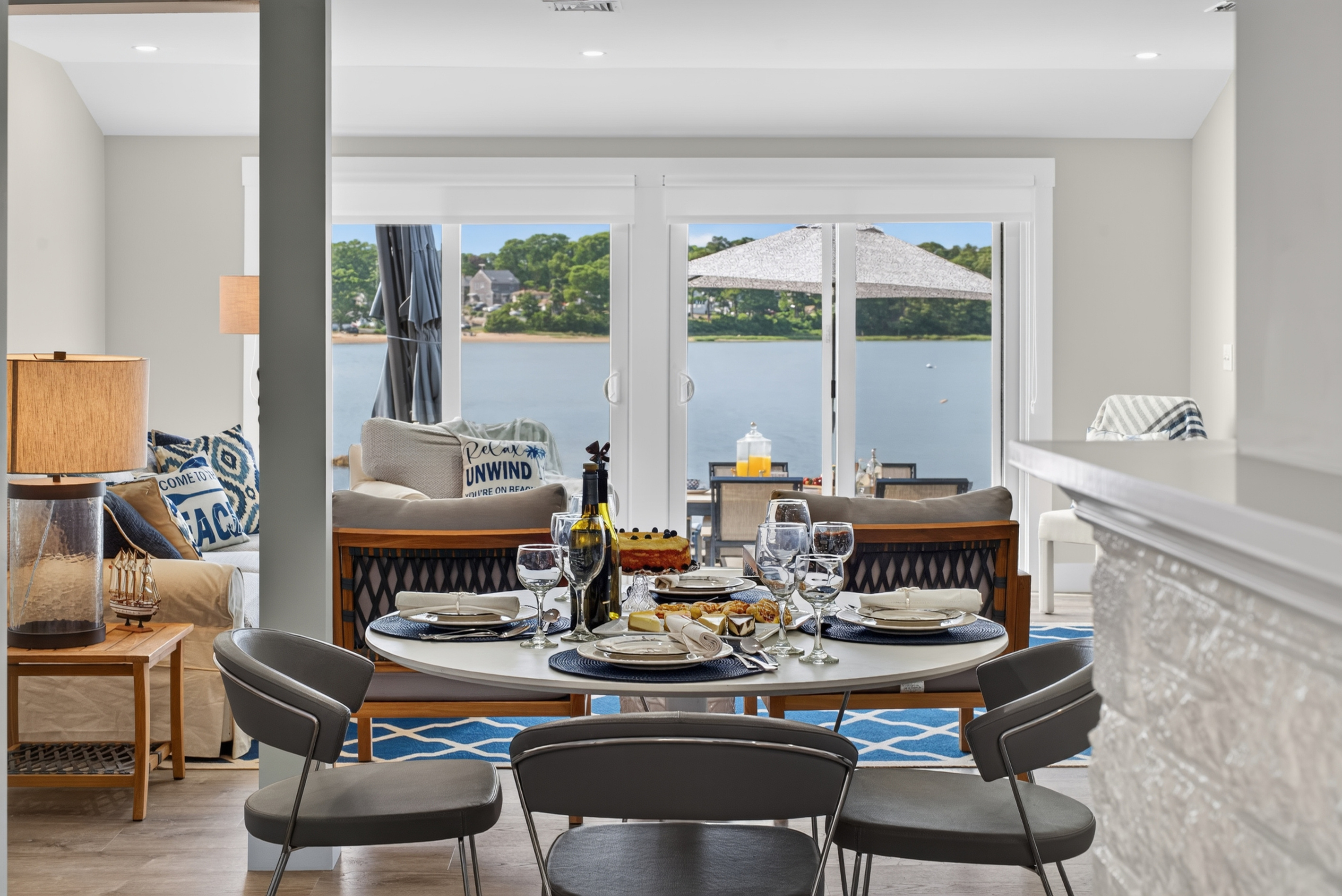 Bright open-concept living and dining area with large windows, comfortable seating, and panoramic waterfront scenery.