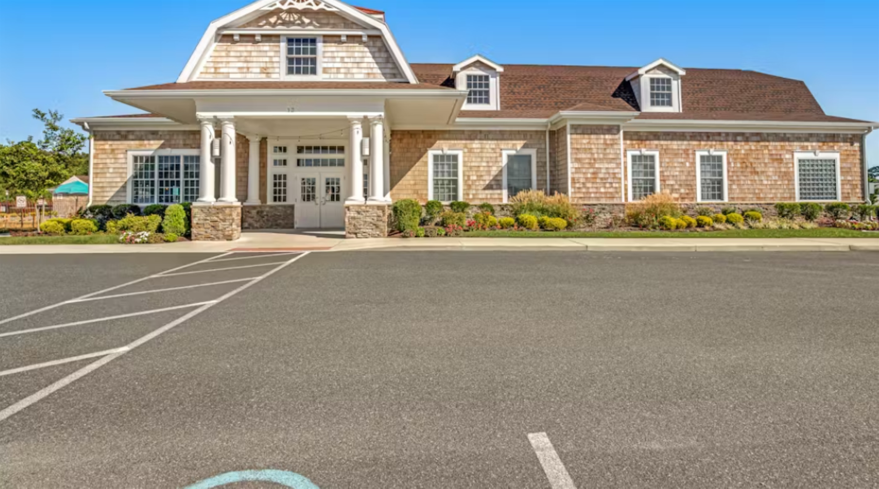 Welcoming clubhouse facade with covered entry, stone accents, and ample guest parking—your hub for community amenities.