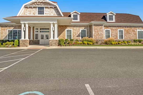 Welcoming clubhouse facade with covered entry, stone accents, and ample guest parking—your hub for community amenities.