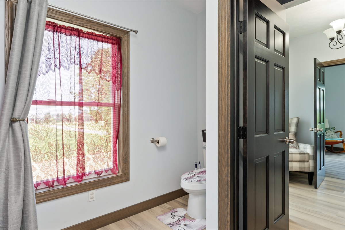 Bright and welcoming with natural light, this second floor bathroom features thoughtful details like lace curtains and matching décor for a cozy, inviting touch.