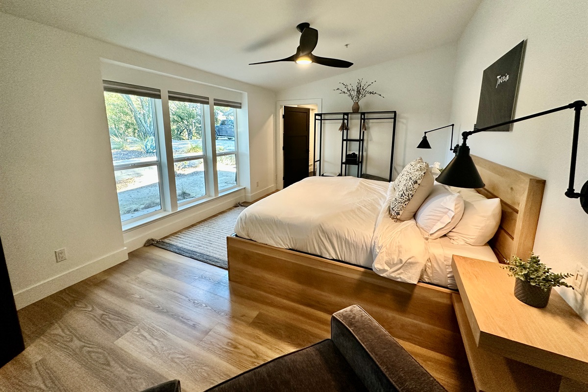 A light-filled king retreat framed by expansive windows, offering a puffy mattress and a minimalist open wardrobe for a boutique-inspired stay.