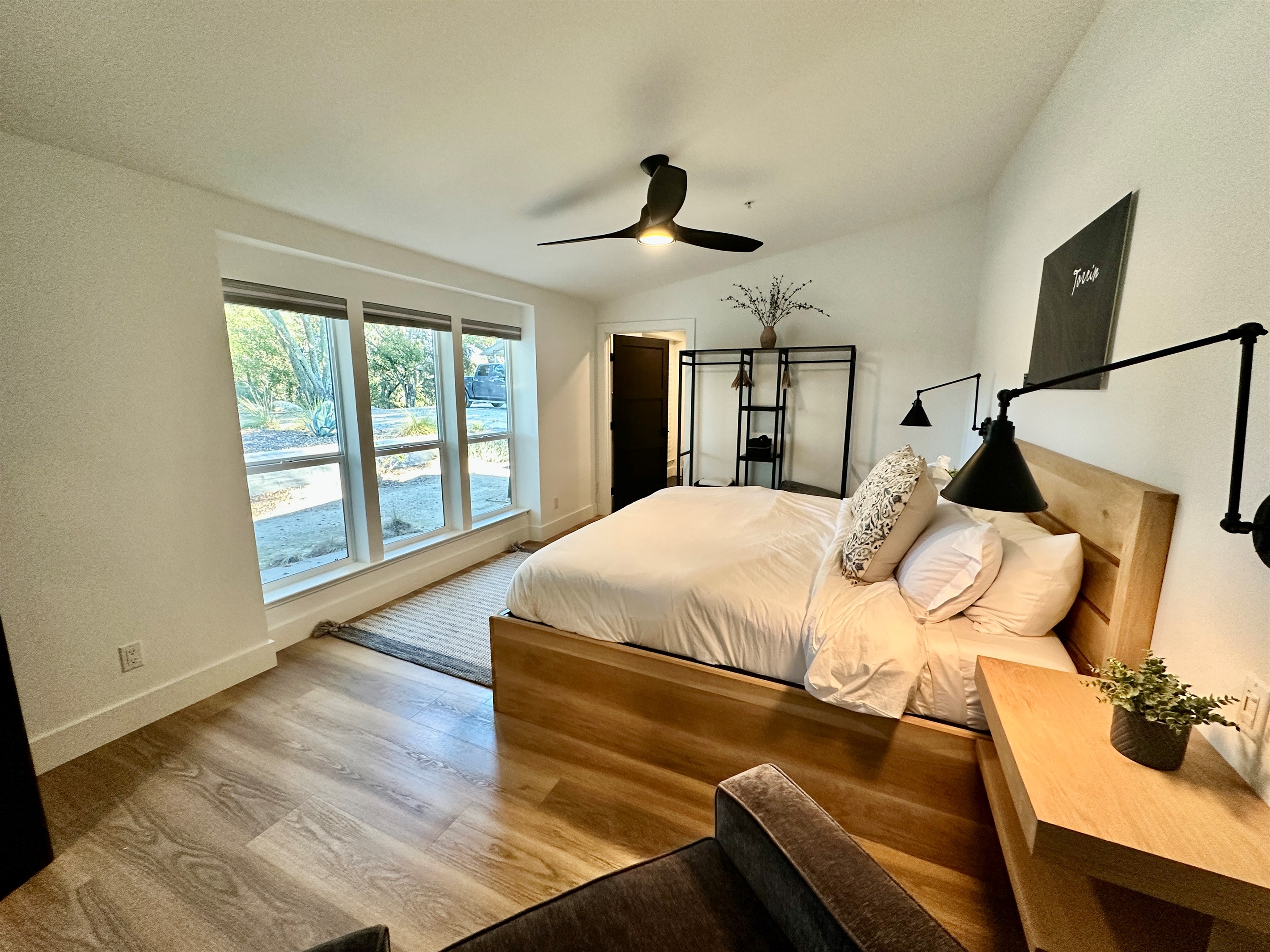 A light-filled king retreat framed by expansive windows, offering a puffy mattress and a minimalist open wardrobe for a boutique-inspired stay.