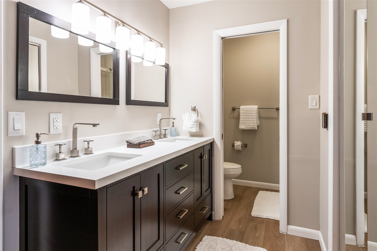 Elegant bathroom with dual sinks, modern lighting, and a separate toilet area, offering comfort and convenience for guests.