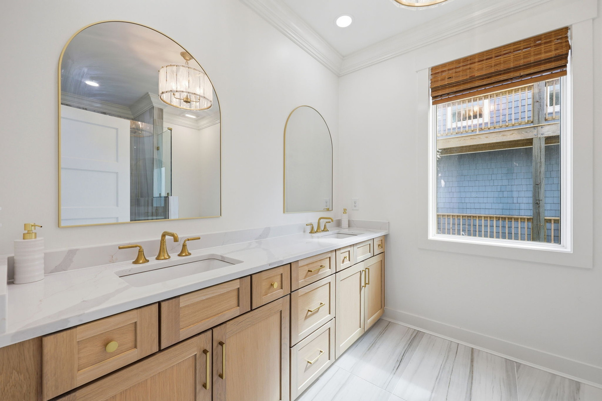 Dual vanity bathroom with wood cabinetry, gold fixtures, and arched mirrors in a bright modern design