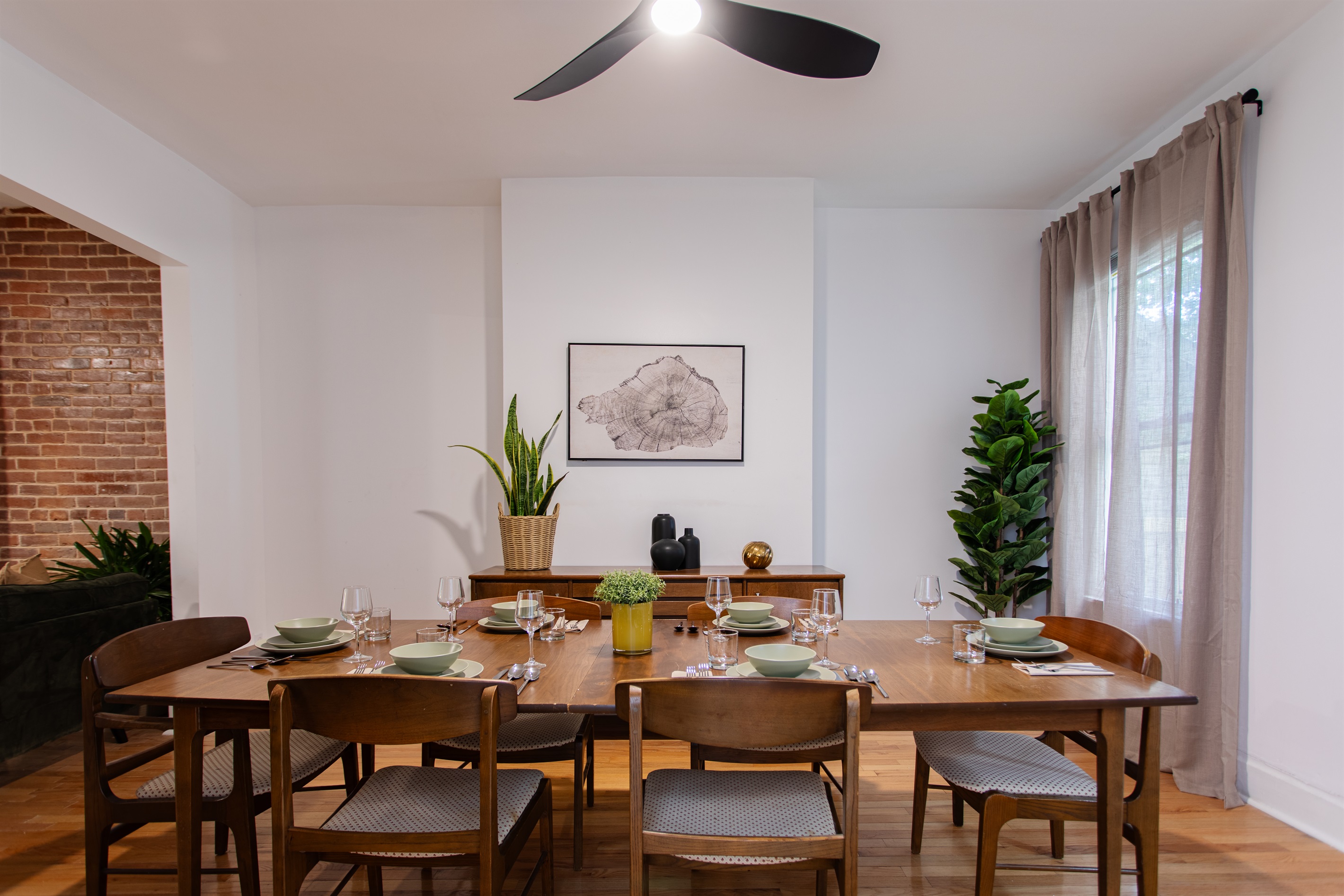 Spacious dining room with a mid-century table for six, accented by natural light, greenery, and simple modern décor.