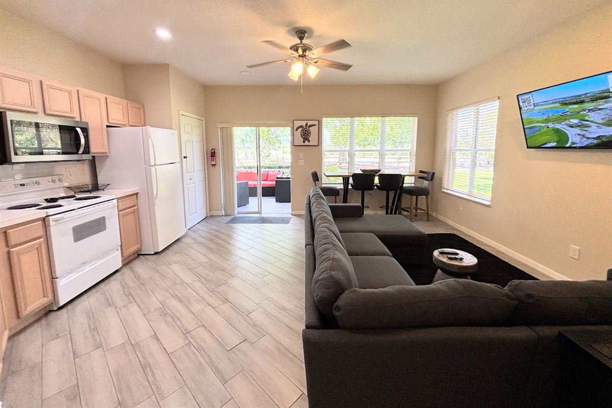 Bright open-concept kitchen and living area with wood-look flooring, comfortable seating, and easy access to the screened patio.