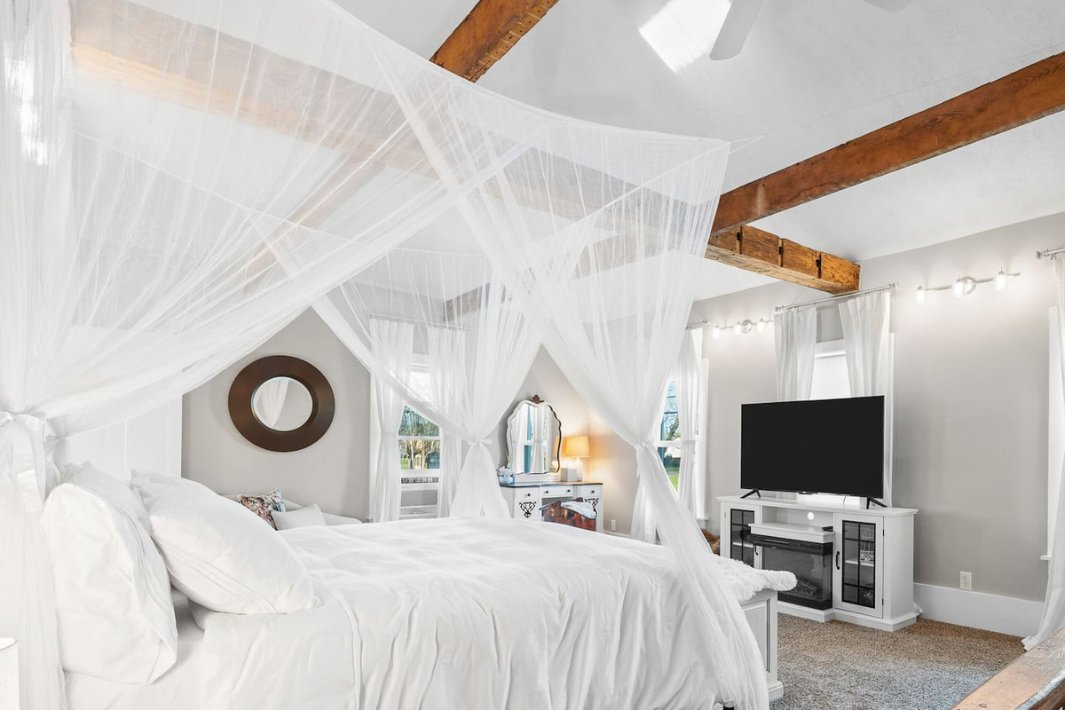 Primary suite with a king canopy bed, exposed beams, and a lighted window cupola overhead.