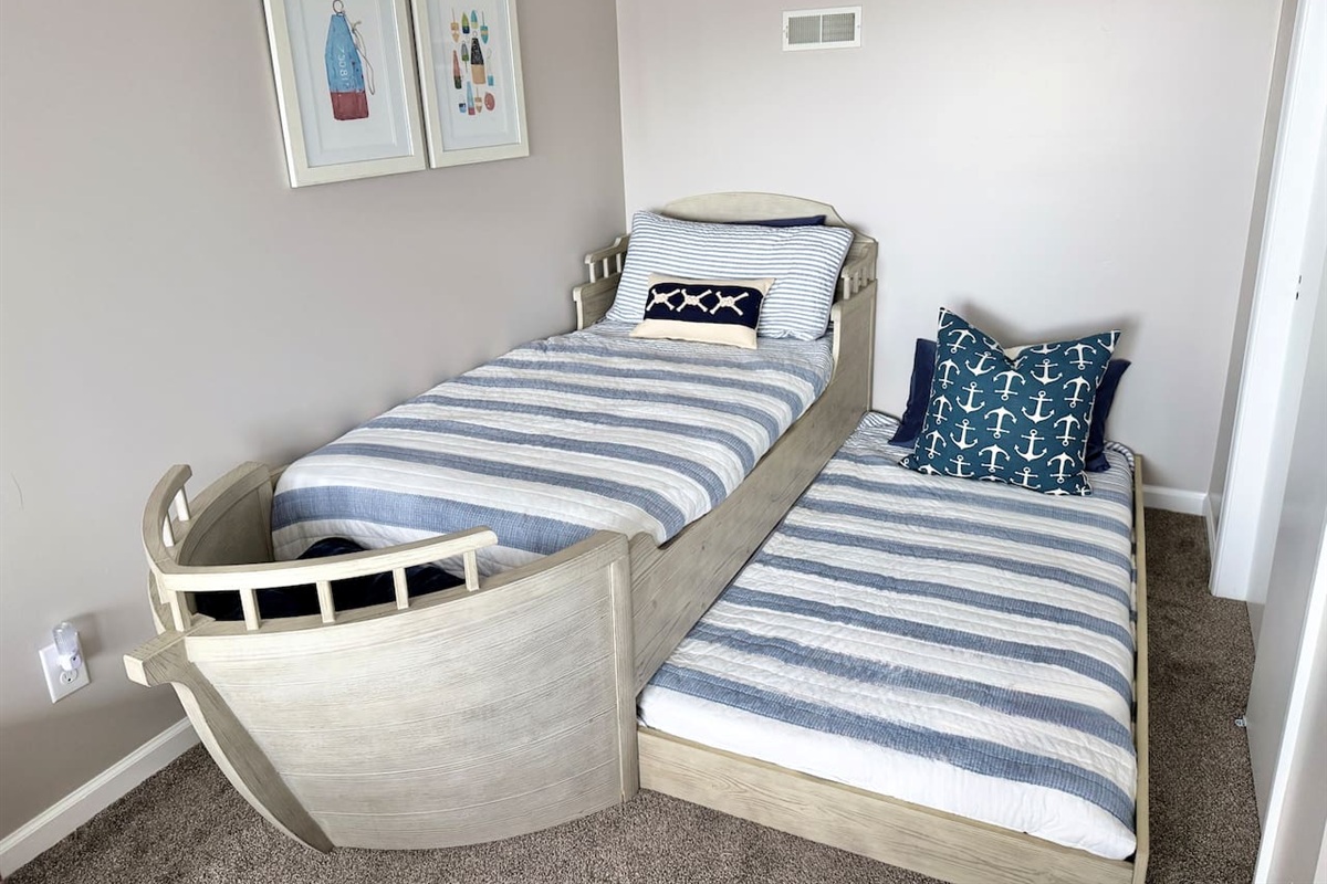 The children will love this charming kid-friendly bedroom features a unique boat-shaped bed complete with a pull-out trundle. The beds are dressed in coordinating blue and white striped quilts and accented with nautical-themed pillows.