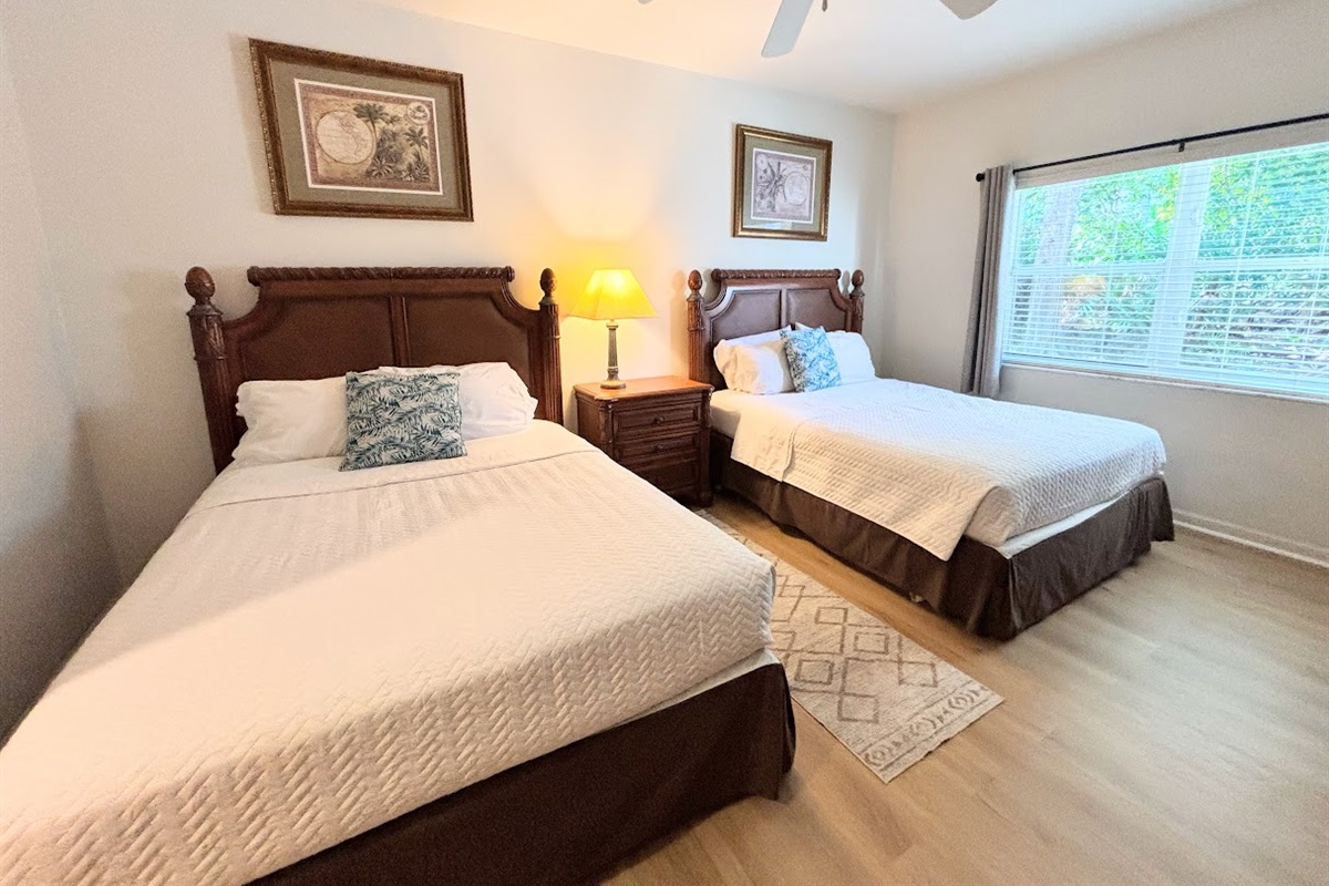 Inviting bedroom featuring two beds, wood-look flooring, ceiling fan, and a bright window view.