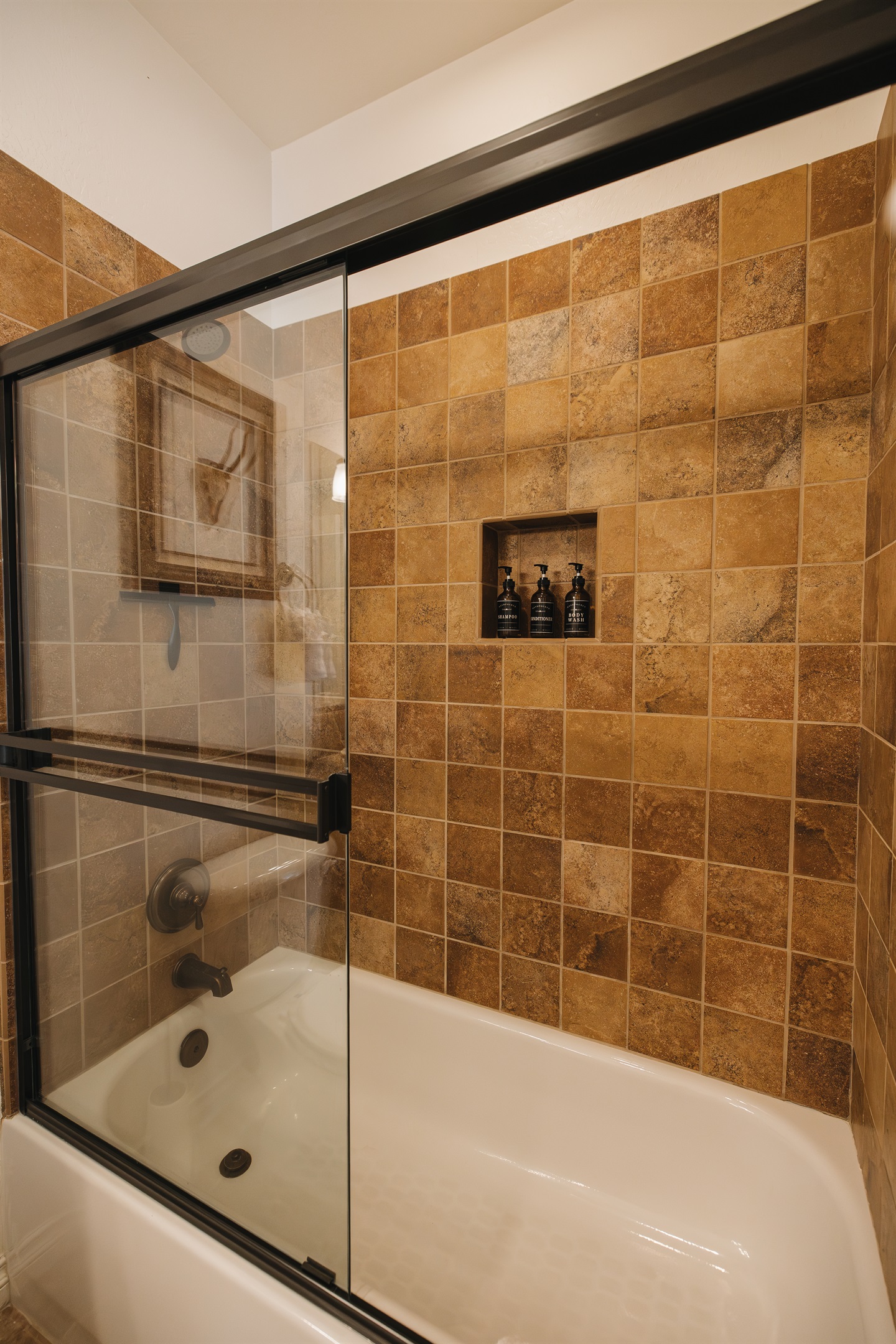 Clean, spa-inspired tub/shower combo with glass doors, warm tile, and built-in niche stocked with essentials—perfect for relaxing after skiing, hiking, or a day exploring the White Mountains.
